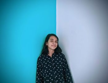 Portrait of smiling young woman standing against wall