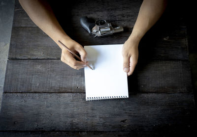 Close-up of businessman writing in note pad with gun on table 