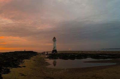 Lighthouse by sea against sky during sunset