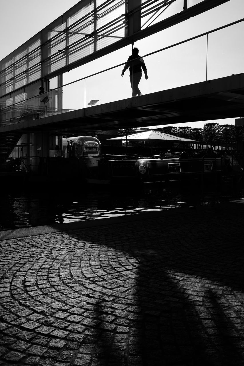 architecture, built structure, city, sky, street, nature, bridge, real people, shadow, building exterior, bridge - man made structure, transportation, day, silhouette, outdoors, one person, walking, footpath, sunlight, cobblestone, paving stone