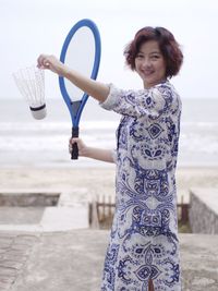 Portrait of smiling woman playing badminton against sea and sky