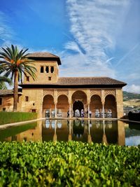 View of alhambra by lake against cloudy sky