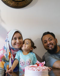 Portrait of smiling family by cake against wall at home