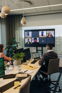 Male and female colleagues looking at tv screen during video conference in coworking office