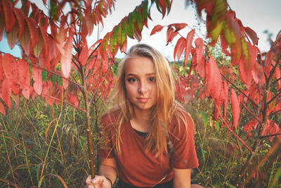 Portrait of young woman by plants at park during sunset