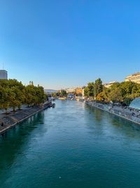 Scenic view of river amidst buildings against clear blue sky