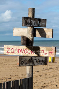 Information sign on wooden post at beach against sky