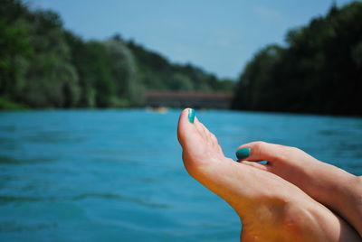 Low section of woman relaxing by lake against blue sky during sunny day