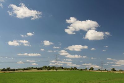 Electricity pylon on field against cloudy sky