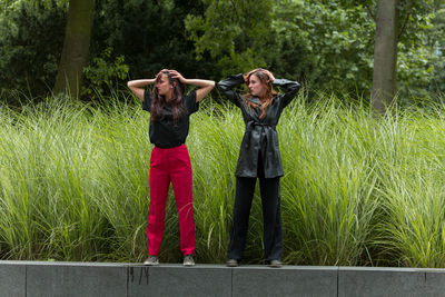 Female friends with hands behind head standing against plants