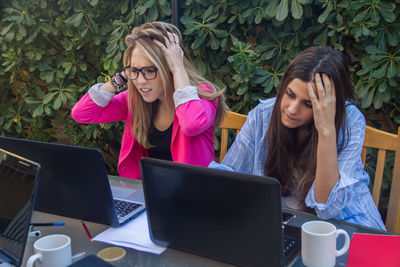 Tensed female colleagues using laptop against plants