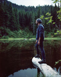 Full length of man standing on fallen tree over lake