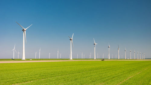 Windmills on field against clear blue sky