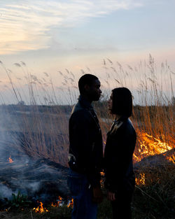 Rear view of a couple standing against trees during sunset