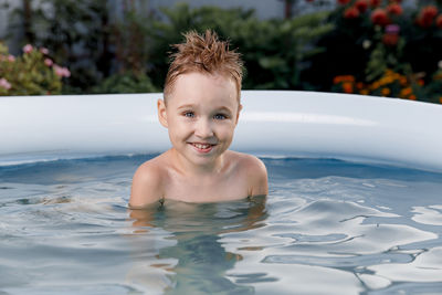Close-up portrait of a smiling five-year-old boy having fun in a blue pool outside on a sunny day