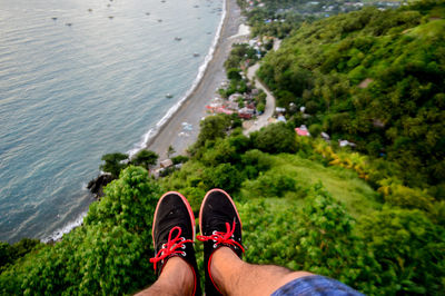 Low section of man sitting on mountain against beach