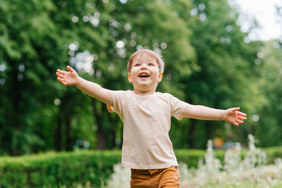 Happy little boy runs with his arms outstretched through the park in summer