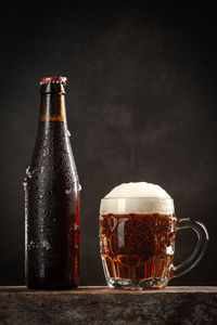 Bottle and jug of beer on wooden base on dark background. vertical format.