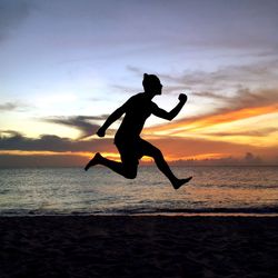 Silhouette man jumping on beach against sky during sunset