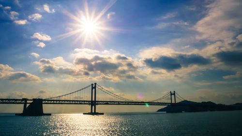 View of suspension bridge over river against cloudy sky