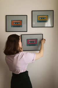 Anonymous female adjusting frame with cassette tape picture on beige wall at home