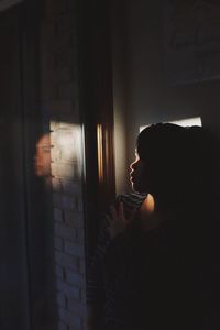 Side view portrait of a serious young woman holding wall at home