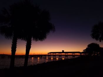 Silhouette palm trees by sea against sky during sunset