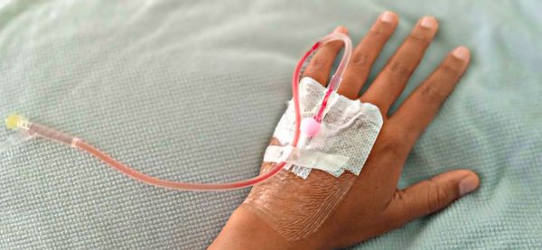 Cropped hand of woman with iv drip on bed