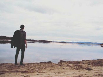 Rear view of man standing on beach against sky