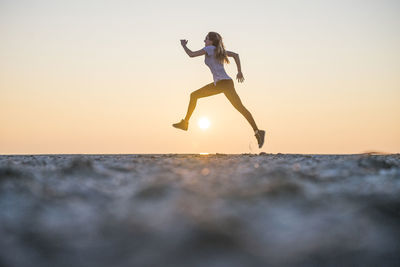 Surface level of woman jumping on sand at beach against clear sky