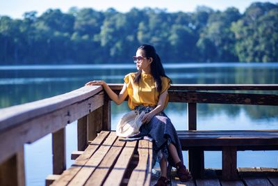 Woman wearing sunglasses looking away while sitting by lake