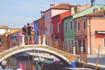 Friends standing on arch bridge over canal by buildings