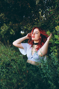 Beautiful young woman with redhead looking away while sitting amidst plants in park