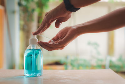 Midsection of woman holding glass bottle on table