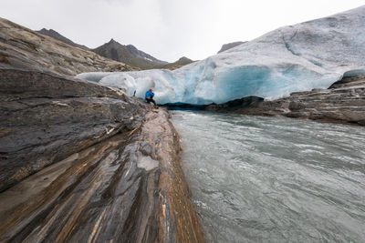 Mid distance of man sitting by glacier against sky