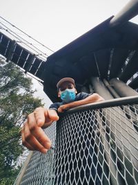Low angle view of boy on metal fence against sky