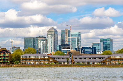 Buildings by river against sky in city