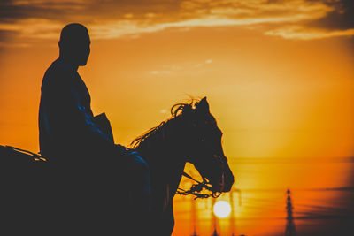 Silhouette man sitting on horse against orange sky