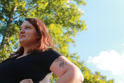 Portrait of beautiful young woman looking away against trees