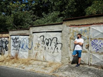 Man with arms crossed leaning against graffiti wall