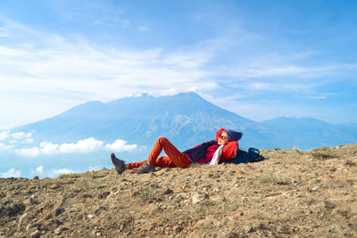 Man relaxing on mountain against sky