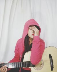 Young woman with eyes closed wearing hooded shirt while holding guitar