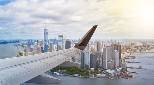 Cropped image of airplane wing flying over river by sea