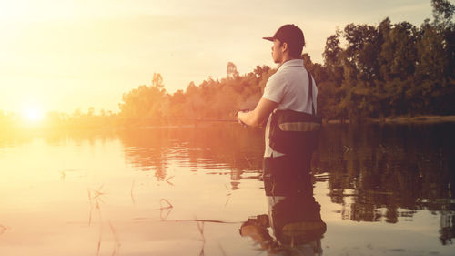 Man standing by lake against sky during sunset