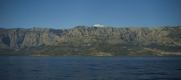 Scenic view of sea and mountains against clear blue sky
