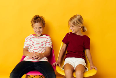 Full length of young woman sitting on sofa against yellow background