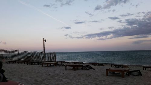 Tables arranged at sandy beach against sky during sunset