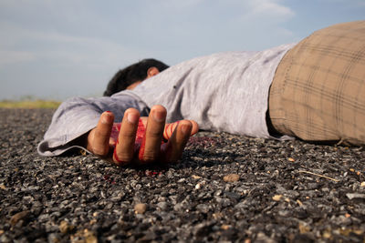 Close-up of man lying down on road against sky