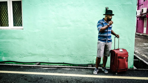 Full length of young man with luggage standing against wall