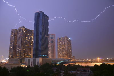 Low angle view of buildings against sky in city during lightning